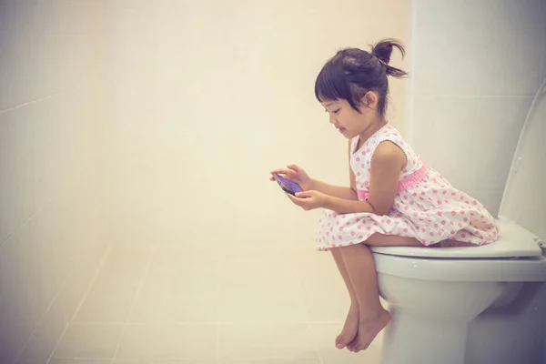 Asian children sitting on a toilet and holding smartphone. — Stock Photo, Image