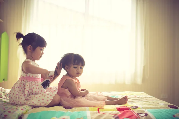 Lovely little girl brushing hair of her sister while sitting on — Stock Photo, Image