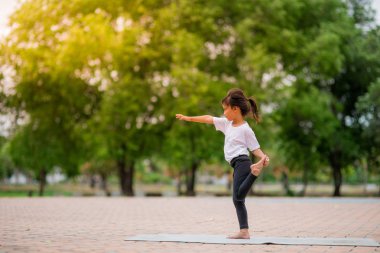 Küçük sevimli asya kız yoga yoga parkta bir paspas üzerinde poz, O