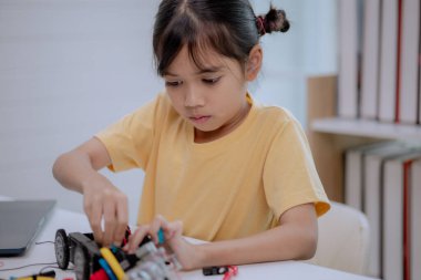 Asian girl assembling electronic parts of robot car, focusing on STEM education and robotics engineering. Concept of child creativity, innovation, technology learning and future development.