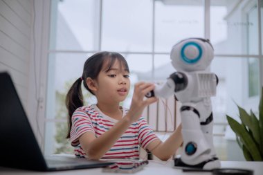 Asian girl interacting with humanoid robot at home, learning STEM education and robotics technology. Concept of child creativity, coding, artificial intelligence and future digital learning.