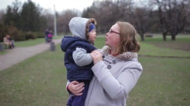 Anne kucağında bir bebek ile parkta, çocuk önünde bir parmak gösterir