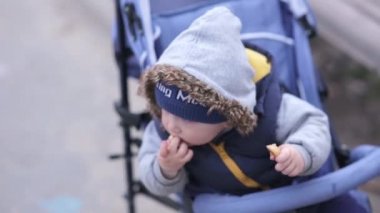 Örme şapkalı mavi gözlü ve kürklü bir kapüşonlu bir çocuk bebek arabasında tatlı yer.