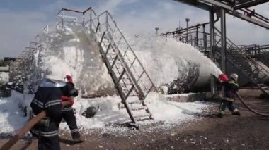 Üç itfaiyeci köpük ile bir tank çiftliğinde bir yangın söndürmek