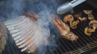 Izgaraya genç buzağı eti pişirmek. Maşalı bir aşçı kızarmış iştah açıcı eti ters çeviriyor..