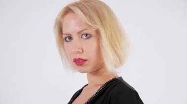 Yakın çekim portre. Yeşil gözlü ve kısa beyaz saçlı siyah tulumlu bir kız beyaz bir arka plan üzerinde stüdyoda poz veriyor. Moda, iş, reklam, oyuncu seçimi. Yavaş çekim.