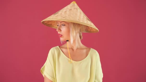 ピンクの背景にポーズの円錐形のわら帽子で緑の目と短い白い髪を持つ美しい女の子 ファッション 中国の帽子 — ストック動画