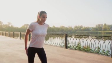 Genç motive olmuş kız yazın parkta koşmaya hazırlanıyor sağlıklı yaşam tarzı, spor anlayışı. Yavaş çekim.