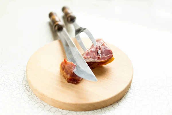 Fork and a large knife for cutting meat or ham are on the cutting boar. Cutting ham or smoked meat.