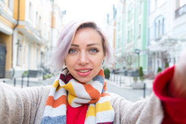 Genç bir kız gülümser ve selfie çeker. Sonbahar gezisi, yürüyüş. Selfie Sokak Fotoğrafı.