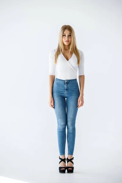 白いシャツと白い背景の上に立ってブルー ジーンズで素敵なブロンドの女の子のスタジオ撮影 — ストック写真