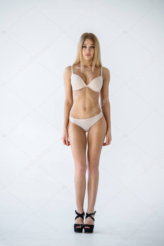 Studio shot of lovely blonde girl in sexy beige lingerie standing on white background