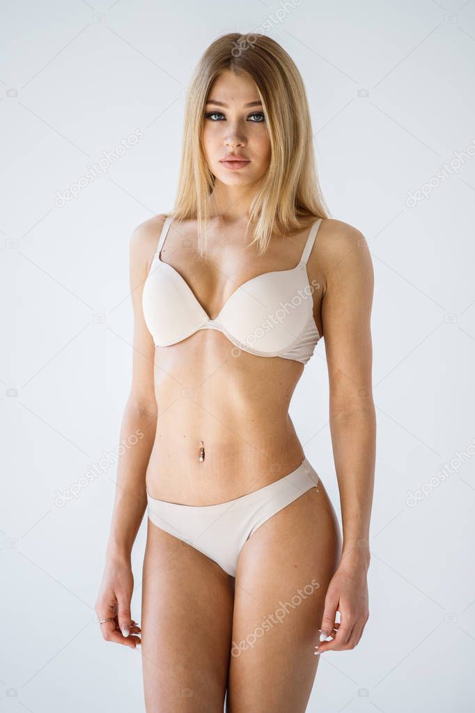 Studio shot of lovely blonde girl in sexy beige lingerie standing on white background