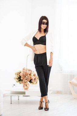 Stüdyo portre siyah pantolon, beyaz ceket ve siyah sütyen evde çiçek kokulu arka plan üzerinde duran güzel esmer kadının yüzünde siyah maske ile 