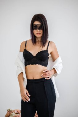 Stüdyo portre siyah pantolon, beyaz ceket ve siyah sütyen evde çiçek kokulu arka plan üzerinde duran güzel esmer kadının yüzünde siyah maske ile 