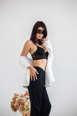 Stüdyo portre siyah pantolon, beyaz ceket ve siyah sütyen evde çiçek kokulu arka plan üzerinde duran güzel esmer kadının yüzünde siyah maske ile 