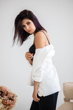 Siyah pantolon, beyaz ceket ve siyah sütyen evde çiçek buketi arka plan üzerinde ayakta giyen güzel esmer kadın portresi stüdyo 