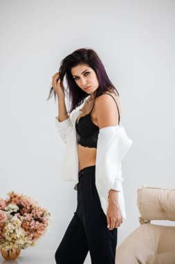 Siyah pantolon, beyaz ceket ve siyah sütyen evde çiçek buketi arka plan üzerinde ayakta giyen güzel esmer kadın portresi stüdyo 