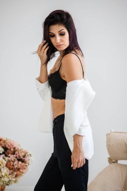 Siyah pantolon, beyaz ceket ve siyah sütyen evde çiçek buketi arka plan üzerinde ayakta giyen güzel esmer kadın portresi stüdyo 