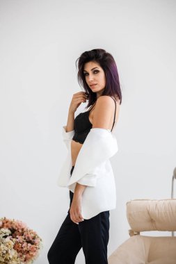 Siyah pantolon, beyaz ceket ve siyah sütyen evde çiçek buketi arka plan üzerinde ayakta giyen güzel esmer kadın portresi stüdyo 