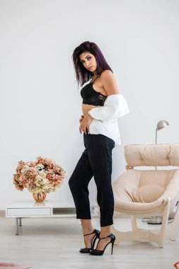 Siyah pantolon, beyaz ceket ve siyah sütyen evde çiçek buketi arka plan üzerinde ayakta giyen güzel esmer kadın portresi stüdyo 