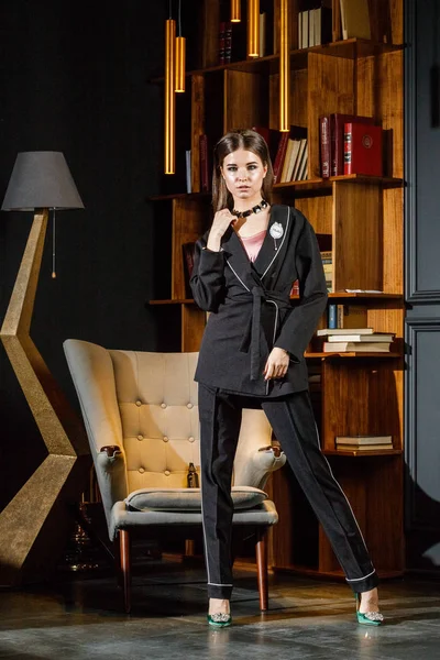 Kitaplık üzerinde arka plan ile ev iç pembe tişört ve siyah takım ayakta giyen güzel esmer kadın portresi 