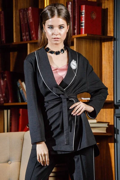 Kitaplık üzerinde arka plan ile ev iç pembe tişört ve siyah takım ayakta giyen güzel esmer kadın portresi 