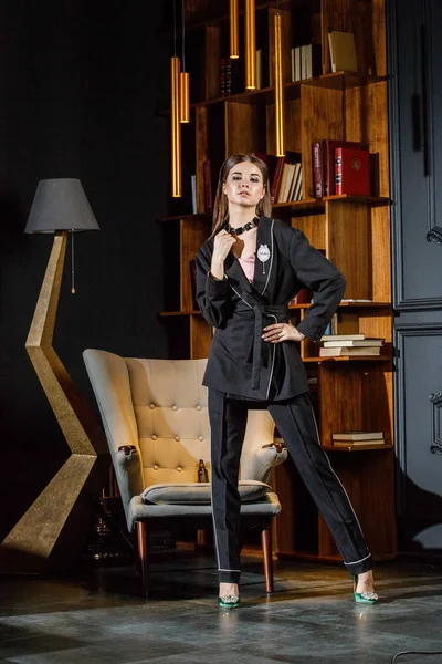 Kitaplık üzerinde arka plan ile ev iç pembe tişört ve siyah takım ayakta giyen güzel esmer kadın portresi 