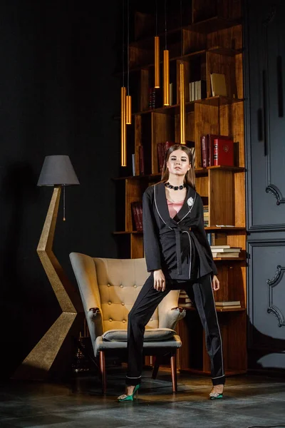 Kitaplık üzerinde arka plan ile ev iç pembe tişört ve siyah takım ayakta giyen güzel esmer kadın portresi 