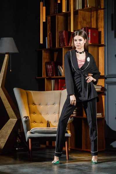 Kitaplık üzerinde arka plan ile ev iç pembe tişört ve siyah takım ayakta giyen güzel esmer kadın portresi 