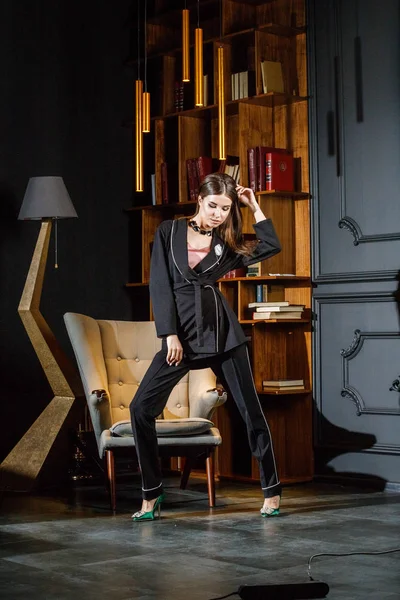 Kitaplık üzerinde arka plan ile ev iç pembe tişört ve siyah takım ayakta giyen güzel esmer kadın portresi 