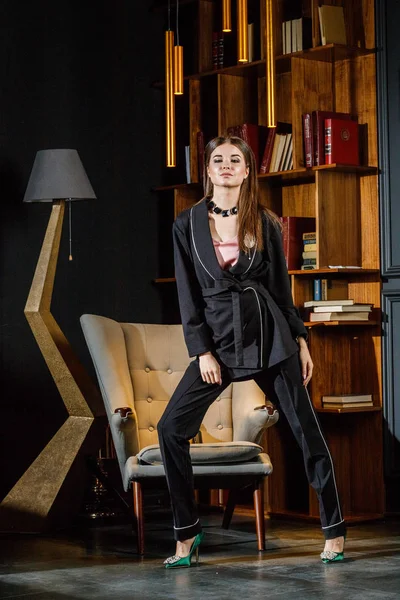 Kitaplık üzerinde arka plan ile ev iç pembe tişört ve siyah takım ayakta giyen güzel esmer kadın portresi 