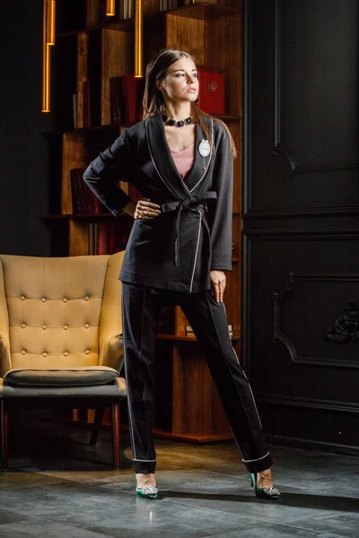 Kitaplık üzerinde arka plan ile ev iç pembe tişört ve siyah takım ayakta giyen güzel esmer kadın portresi 