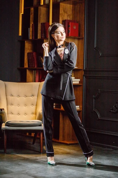 Kitaplık üzerinde arka plan ile ev iç pembe tişört ve siyah takım ayakta giyen güzel esmer kadın portresi 