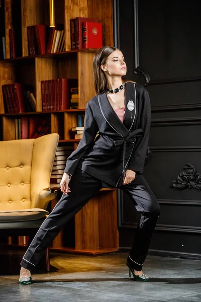 Kitaplık üzerinde arka plan ile ev iç pembe tişört ve siyah takım ayakta giyen güzel esmer kadın portresi 