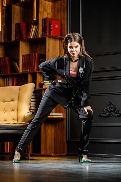 Kitaplık üzerinde arka plan ile ev iç pembe tişört ve siyah takım ayakta giyen güzel esmer kadın portresi 