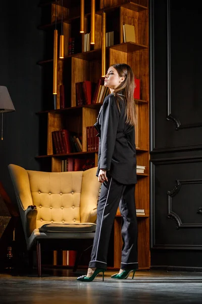 Kitaplık üzerinde arka plan ile ev iç pembe tişört ve siyah takım ayakta giyen güzel esmer kadın portresi 