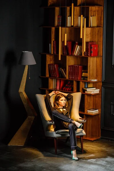 Pembe tişört ve koltuk ile kitaplık arka plan üzerine oturmuş siyah takım elbise giyen güzel esmer kadın portresi 