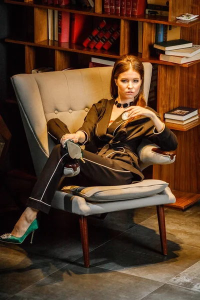 Pembe tişört ve koltuk ile kitaplık arka plan üzerine oturmuş siyah takım elbise giyen güzel esmer kadın portresi 