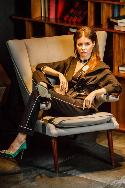 Pembe tişört ve koltuk ile kitaplık arka plan üzerine oturmuş siyah takım elbise giyen güzel esmer kadın portresi 