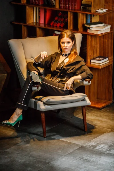 Pembe tişört ve koltuk ile kitaplık arka plan üzerine oturmuş siyah takım elbise giyen güzel esmer kadın portresi 