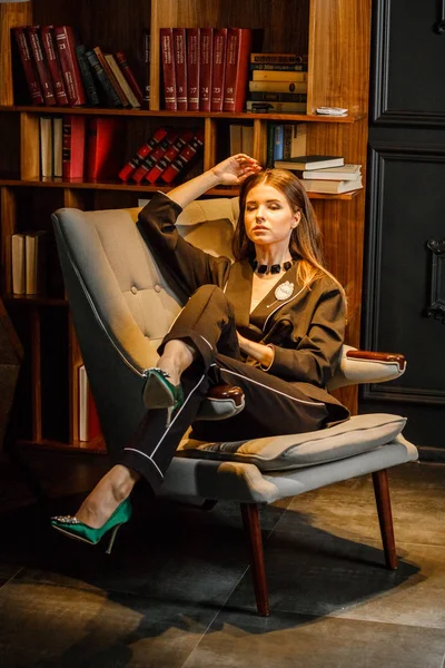 Pembe tişört ve koltuk ile kitaplık arka plan üzerine oturmuş siyah takım elbise giyen güzel esmer kadın portresi 