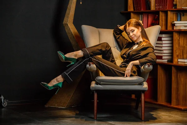 Pembe tişört ve koltuk ile kitaplık arka plan üzerine oturmuş siyah takım elbise giyen güzel esmer kadın portresi 