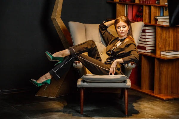 Pembe tişört ve koltuk ile kitaplık arka plan üzerine oturmuş siyah takım elbise giyen güzel esmer kadın portresi 