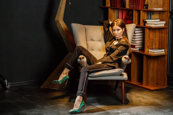 Pembe tişört ve koltuk ile kitaplık arka plan üzerine oturmuş siyah takım elbise giyen güzel esmer kadın portresi 