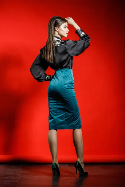 在红色背景的休闲服装的年轻模特的工作室肖像 穿黑色衬衣和蓝色裙子的年轻妇女在演播室摆姿势 — 图库照片