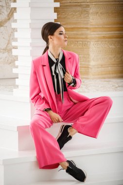 Pembe takım elbise ve lüks ev iç merdiven üzerinde oturan siyah t-shirt giyen güzel esmer kadın portresi stüdyo 