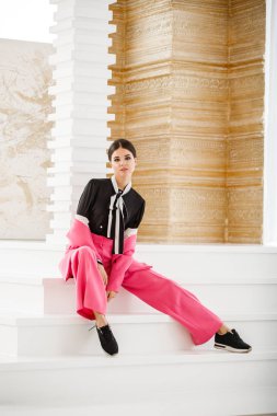 Pembe takım elbise ve lüks ev iç merdiven üzerinde oturan siyah t-shirt giyen güzel esmer kadın portresi stüdyo 