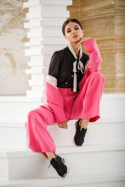 Pembe takım elbise ve lüks ev iç merdiven üzerinde oturan siyah t-shirt giyen güzel esmer kadın portresi stüdyo 