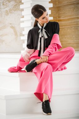 Pembe takım elbise ve lüks ev iç merdiven üzerinde oturan siyah t-shirt giyen güzel esmer kadın portresi stüdyo 